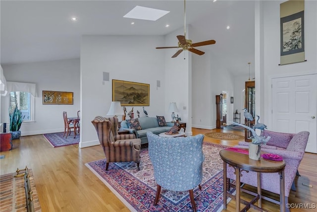 living room featuring ceiling fan, light hardwood / wood-style flooring, high vaulted ceiling, and a skylight