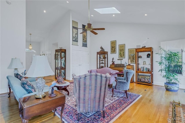 living room featuring a skylight, ceiling fan, light hardwood / wood-style flooring, and high vaulted ceiling