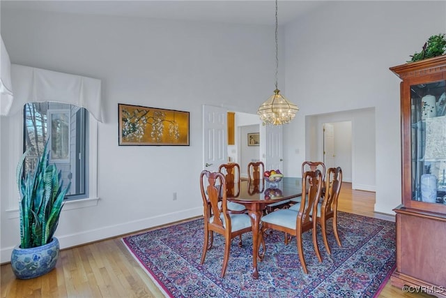 dining room with wood-type flooring, high vaulted ceiling, and an inviting chandelier