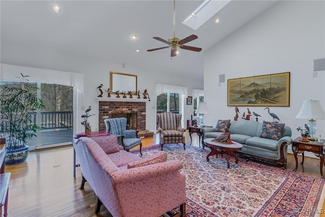 living room featuring a skylight, ceiling fan, a brick fireplace, high vaulted ceiling, and hardwood / wood-style floors