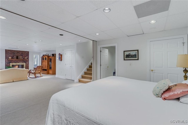 carpeted bedroom featuring a paneled ceiling and a brick fireplace