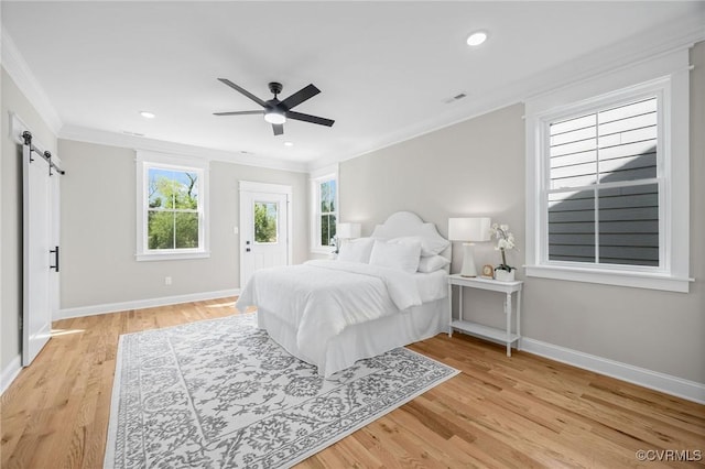 bedroom featuring light hardwood / wood-style flooring, ornamental molding, a barn door, and ceiling fan