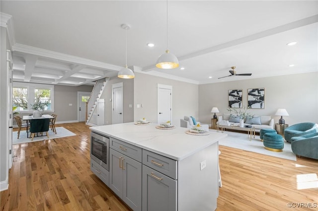 kitchen with coffered ceiling, hanging light fixtures, light wood-type flooring, stainless steel microwave, and beamed ceiling