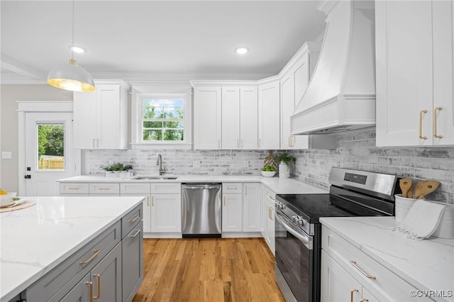 kitchen featuring sink, hanging light fixtures, stainless steel appliances, custom range hood, and white cabinets