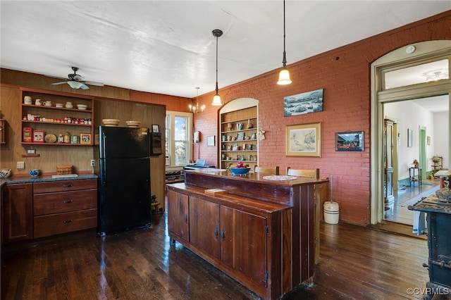 kitchen featuring a center island, dark hardwood / wood-style flooring, decorative light fixtures, black refrigerator, and ceiling fan with notable chandelier