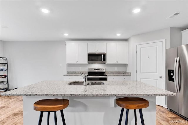 kitchen featuring a kitchen island with sink, a kitchen bar, white cabinetry, and appliances with stainless steel finishes