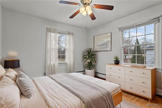 bedroom featuring a baseboard radiator, multiple windows, light hardwood / wood-style floors, and ceiling fan