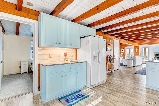 kitchen featuring beamed ceiling, light colored carpet, white fridge with ice dispenser, and blue cabinets