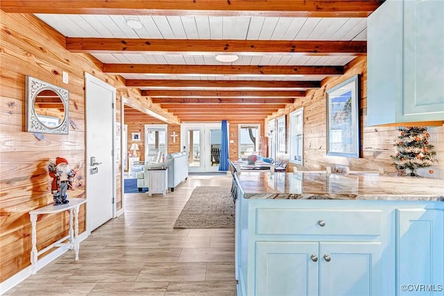 kitchen featuring light stone countertops, beam ceiling, wooden walls, and a healthy amount of sunlight