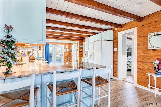 kitchen featuring wood walls, white refrigerator with ice dispenser, light hardwood / wood-style flooring, beam ceiling, and kitchen peninsula