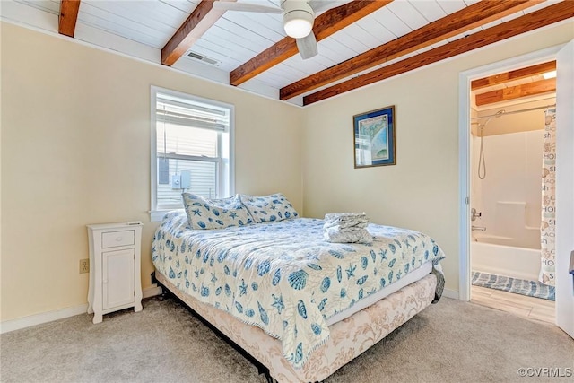 bedroom with beamed ceiling, ceiling fan, light carpet, and ensuite bath