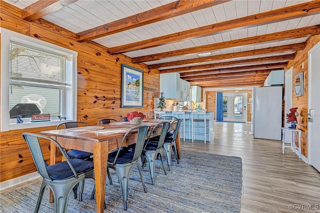 dining space featuring beam ceiling, light hardwood / wood-style floors, wooden walls, and wooden ceiling