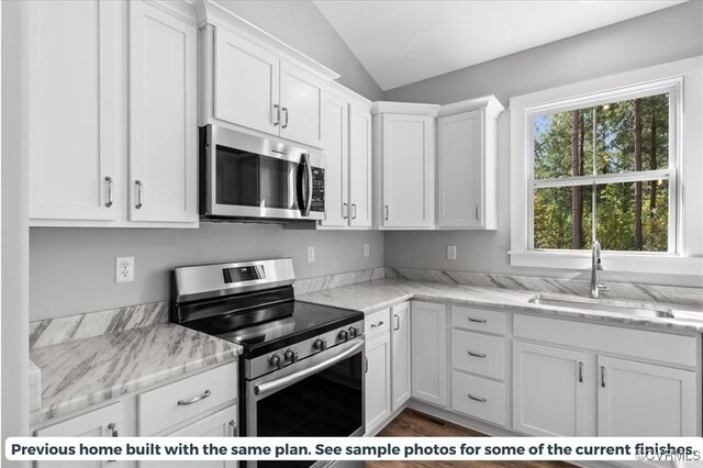 kitchen with stainless steel appliances, sink, white cabinetry, vaulted ceiling, and light stone counters