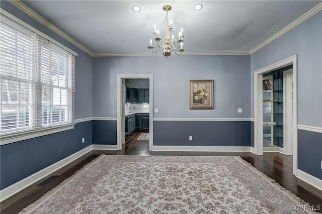 unfurnished room featuring dark hardwood / wood-style floors, ornamental molding, and an inviting chandelier