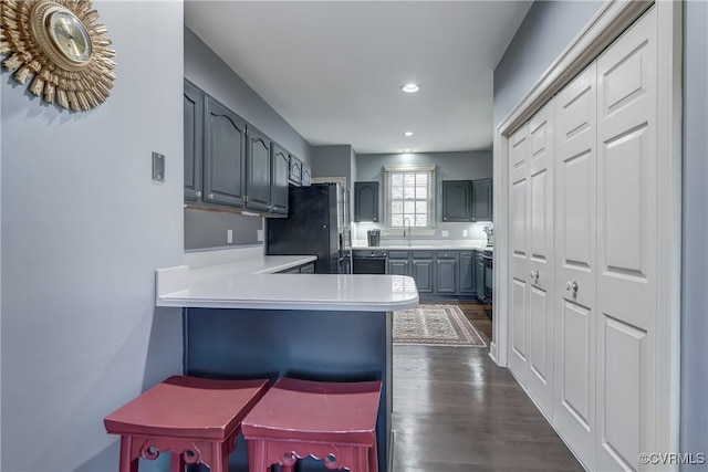 kitchen featuring black appliances, gray cabinets, dark hardwood / wood-style flooring, a kitchen bar, and kitchen peninsula