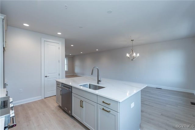 kitchen with sink, light stone counters, light hardwood / wood-style floors, decorative light fixtures, and a kitchen island with sink