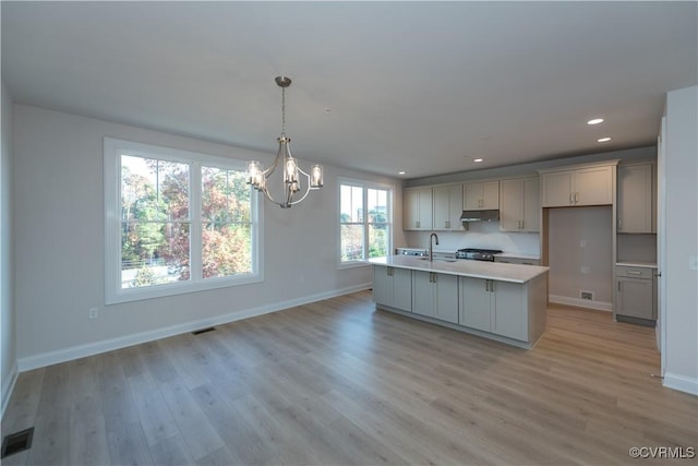 kitchen with sink, hanging light fixtures, an inviting chandelier, a kitchen island with sink, and light wood-type flooring