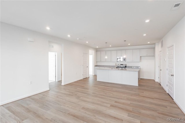 kitchen with pendant lighting, light hardwood / wood-style flooring, an island with sink, appliances with stainless steel finishes, and white cabinetry