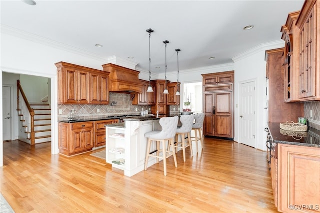 kitchen featuring premium range hood, a kitchen breakfast bar, hanging light fixtures, light wood-type flooring, and a kitchen island