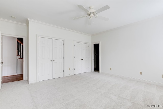 unfurnished bedroom with ceiling fan, ornamental molding, light carpet, and two closets