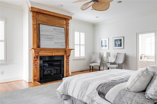 bedroom featuring ensuite bath, ceiling fan, a premium fireplace, light wood-type flooring, and ornamental molding