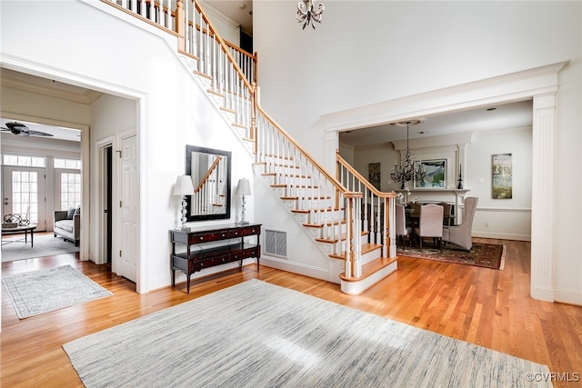 foyer entrance with ceiling fan with notable chandelier, wood-type flooring, ornamental molding, and a towering ceiling