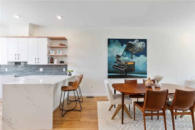 kitchen featuring backsplash, white cabinetry, light hardwood / wood-style floors, and light stone counters