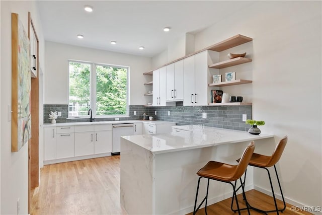 kitchen featuring a breakfast bar, dishwasher, kitchen peninsula, decorative backsplash, and white cabinetry