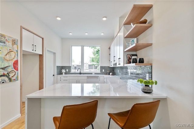 kitchen with a breakfast bar, decorative backsplash, white cabinetry, and kitchen peninsula