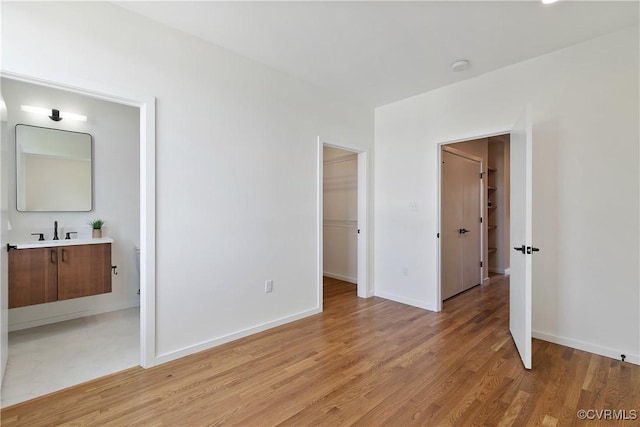 unfurnished bedroom with a closet, a spacious closet, light hardwood / wood-style flooring, and sink