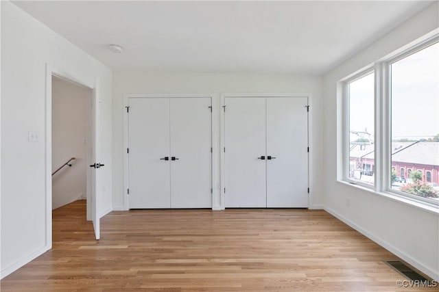 unfurnished bedroom featuring light wood-type flooring and two closets