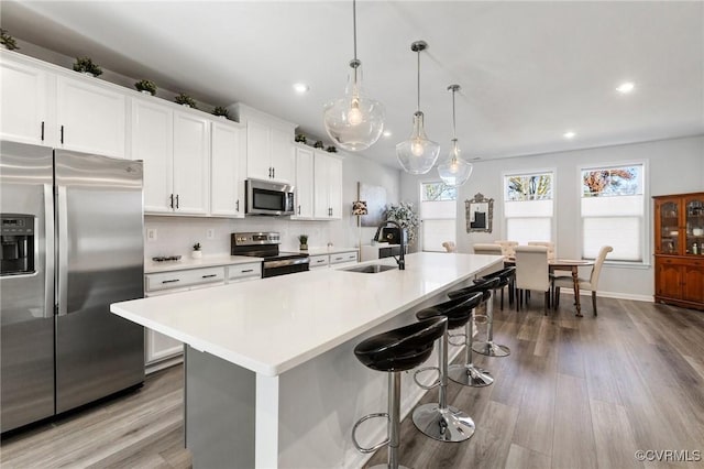 kitchen featuring pendant lighting, light wood-type flooring, stainless steel appliances, and a kitchen island with sink