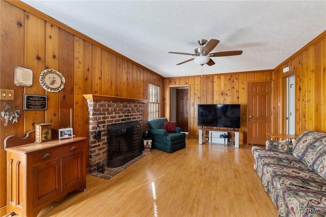 living room with ceiling fan, a brick fireplace, light hardwood / wood-style flooring, crown molding, and wood walls