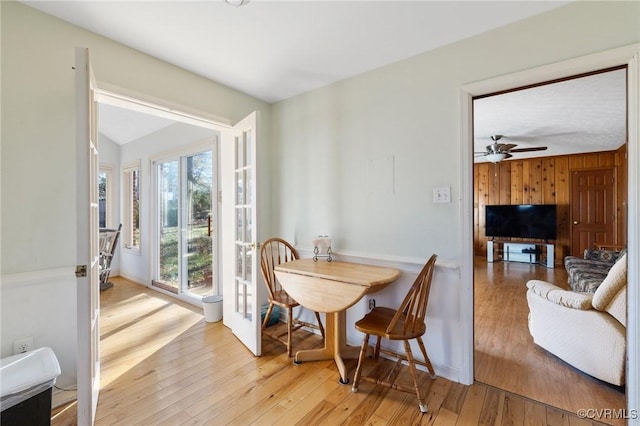 dining room with ceiling fan, wood walls, and light wood-type flooring