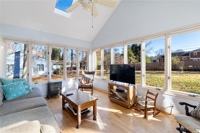 sunroom with a wood stove, lofted ceiling with skylight, and ceiling fan