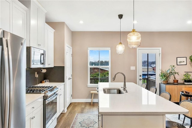 kitchen featuring appliances with stainless steel finishes, light wood-type flooring, a kitchen island with sink, sink, and hanging light fixtures