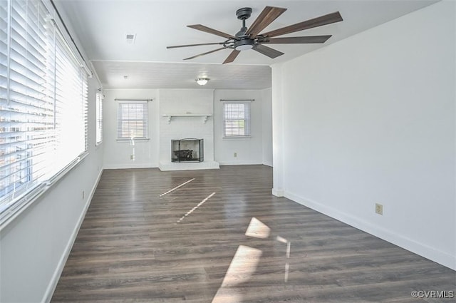 unfurnished living room with a wealth of natural light, dark hardwood / wood-style flooring, ceiling fan, and a brick fireplace