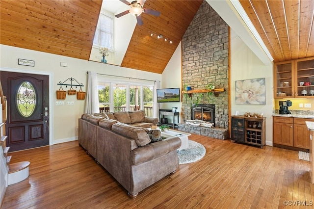 living room with ceiling fan, wooden ceiling, a stone fireplace, high vaulted ceiling, and light wood-type flooring