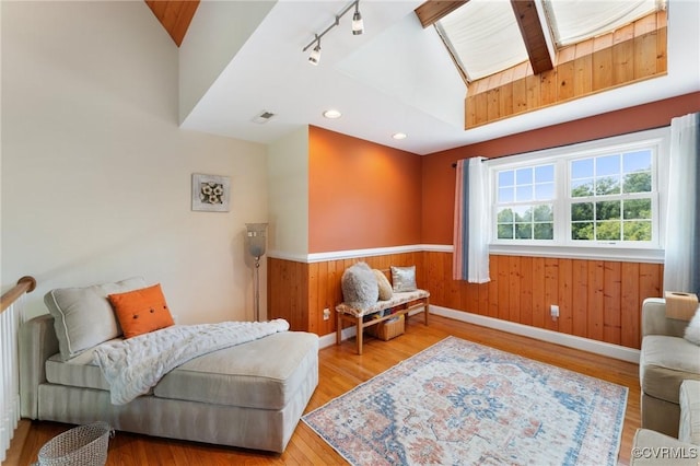 living area featuring wood walls, vaulted ceiling, rail lighting, and light hardwood / wood-style flooring