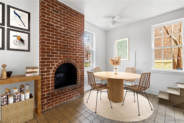 tiled dining room with ceiling fan, a wealth of natural light, and a brick fireplace