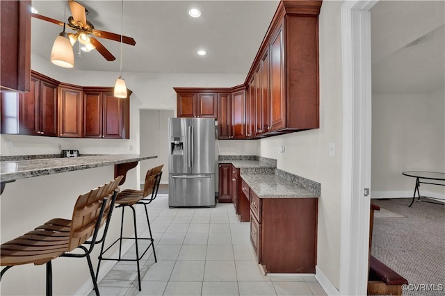 kitchen featuring a kitchen bar, stainless steel refrigerator with ice dispenser, ceiling fan, light tile patterned floors, and stone counters