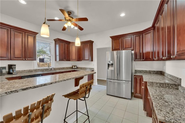 kitchen with light stone countertops, ceiling fan, stainless steel appliances, decorative light fixtures, and a breakfast bar