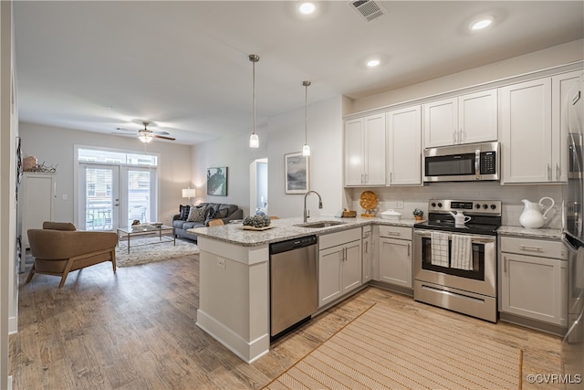 kitchen with appliances with stainless steel finishes, light wood-type flooring, sink, decorative light fixtures, and white cabinets