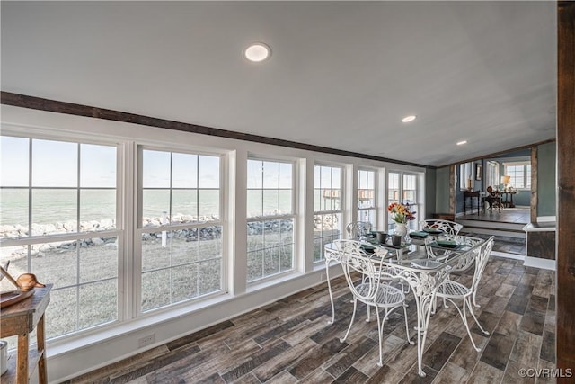 sunroom featuring a water view, a healthy amount of sunlight, lofted ceiling, and a view of the beach