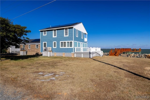 back of house with a deck with water view and a lawn