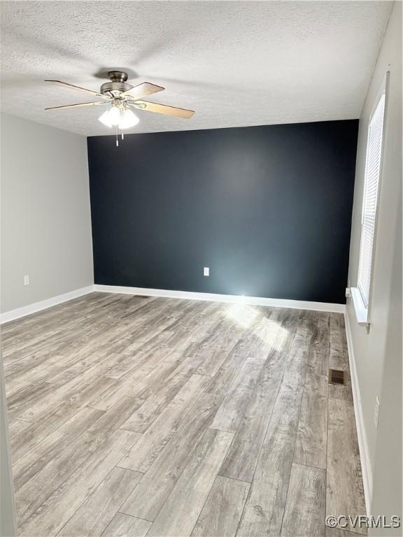 empty room featuring ceiling fan, light hardwood / wood-style floors, and a textured ceiling