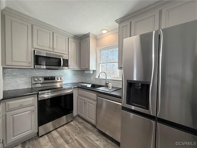 kitchen featuring sink, light hardwood / wood-style flooring, appliances with stainless steel finishes, backsplash, and a textured ceiling