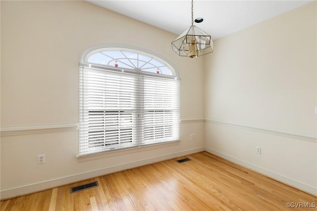 empty room featuring wood-type flooring and a chandelier