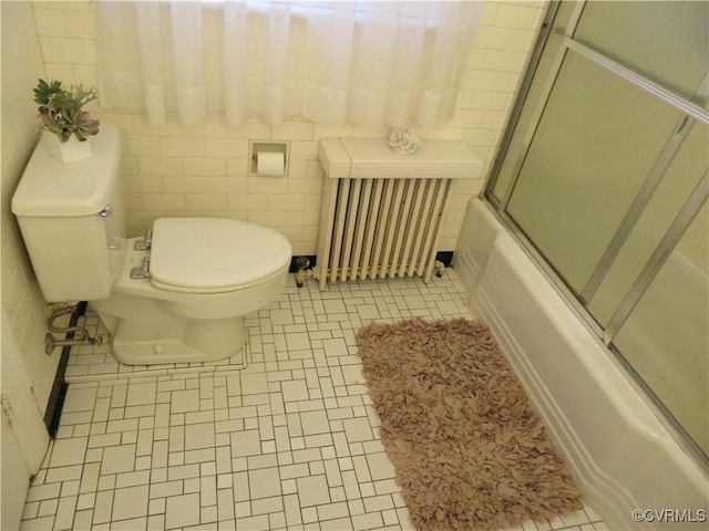 bathroom with radiator, tile patterned floors, toilet, shower / bath combination with glass door, and tile walls