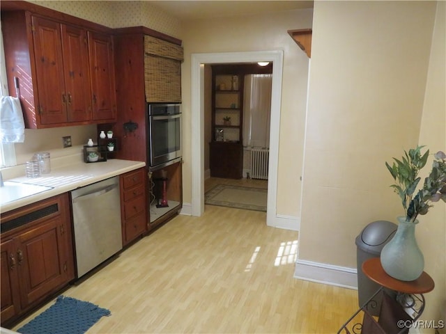 kitchen featuring sink, radiator heating unit, stainless steel appliances, and light wood-type flooring